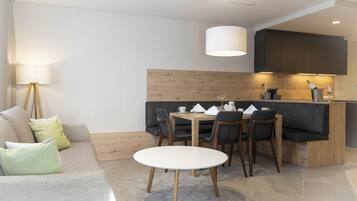 Ein modernes Wohnzimmer mit einer Couch, einem Esstisch mit Stühlen, einer Lampe und einer Küchenzeile mit Schränken und einer Arbeitsplatte.