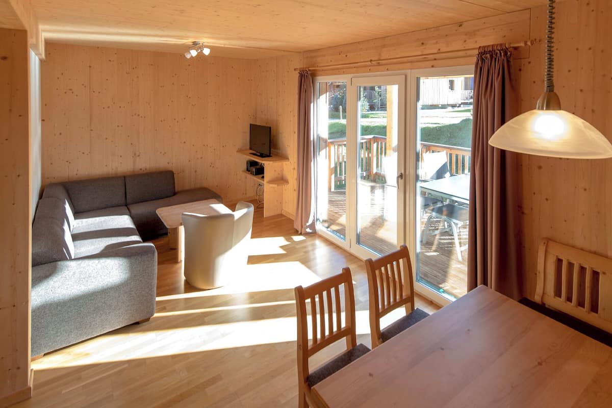 A wooden interior with a sofa, a table, chairs, a TV, and a sliding glass door leading to an outdoor area.