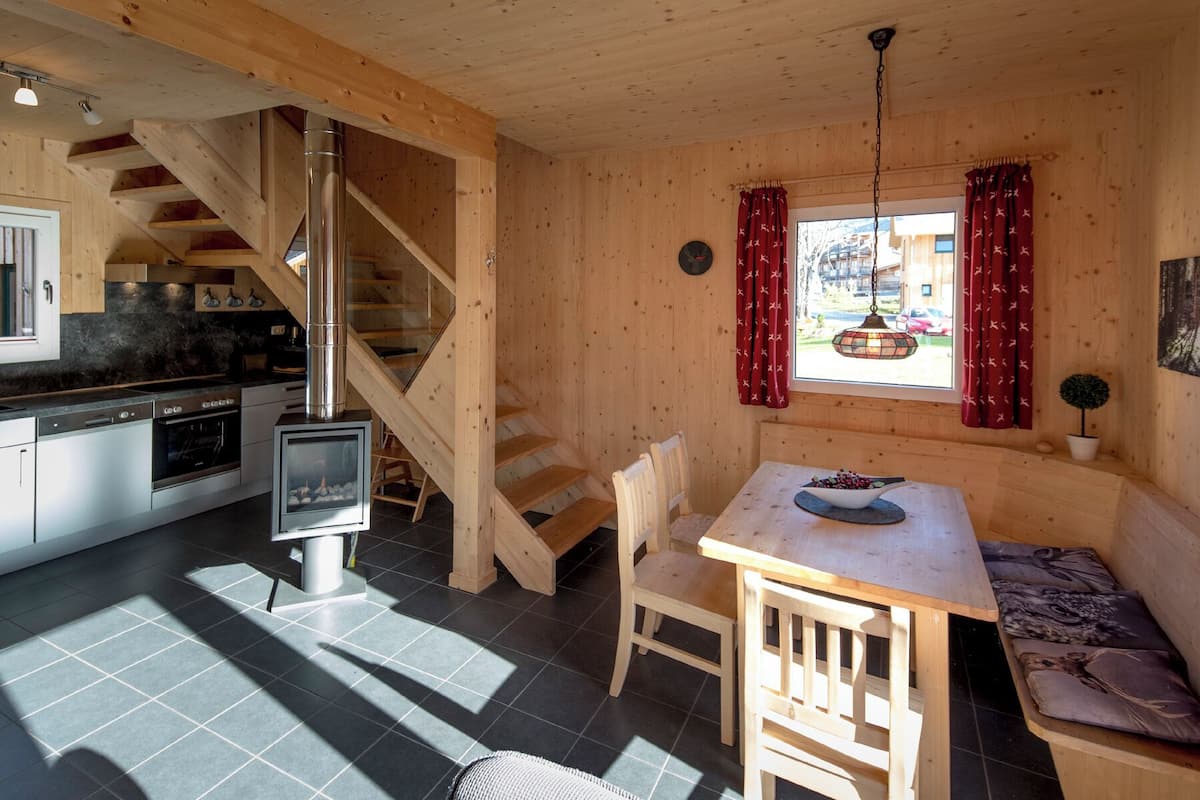 A wooden cabin interior with a kitchen, dining area, and a staircase.