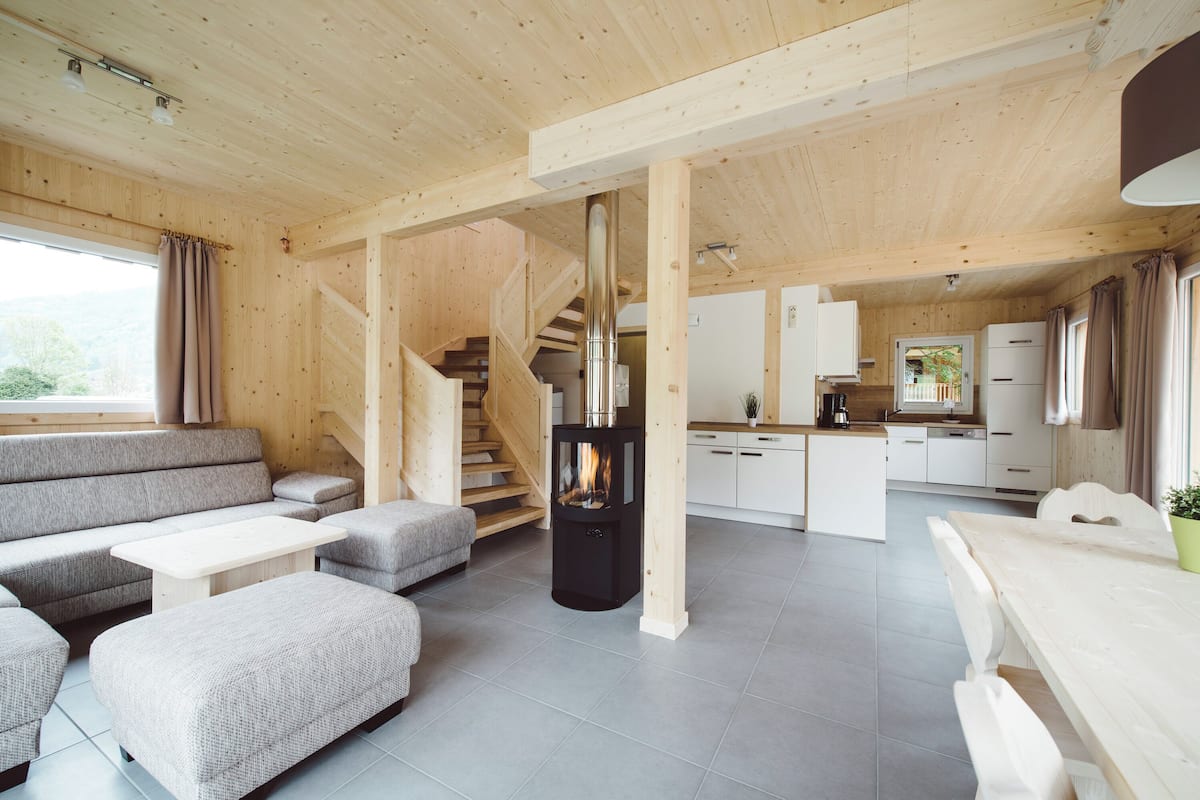 Amplia sala de estar con chimenea, un conjunto de sofás, una mesa de comedor y una cocina al fondo.