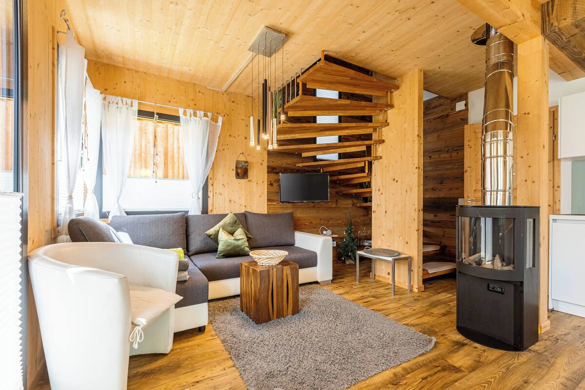 Interior acogedor de una cabaña de madera con sofá, sillón blanco y chimenea.
