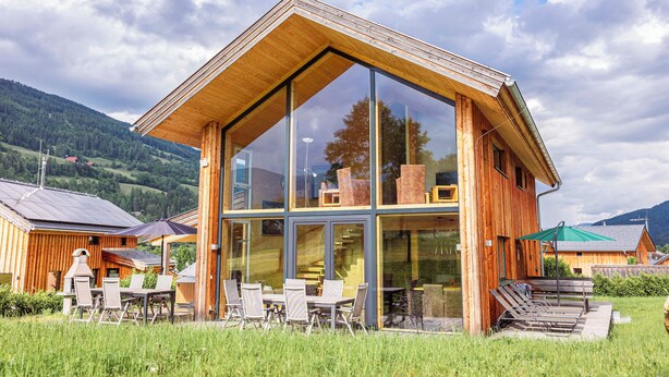 A modern wooden building with large glass windows, outdoor seating, and a view of the surrounding landscape. - Kreischberg Chalets by ALPS RESORTS (Sankt Georgen am Kreischberg)