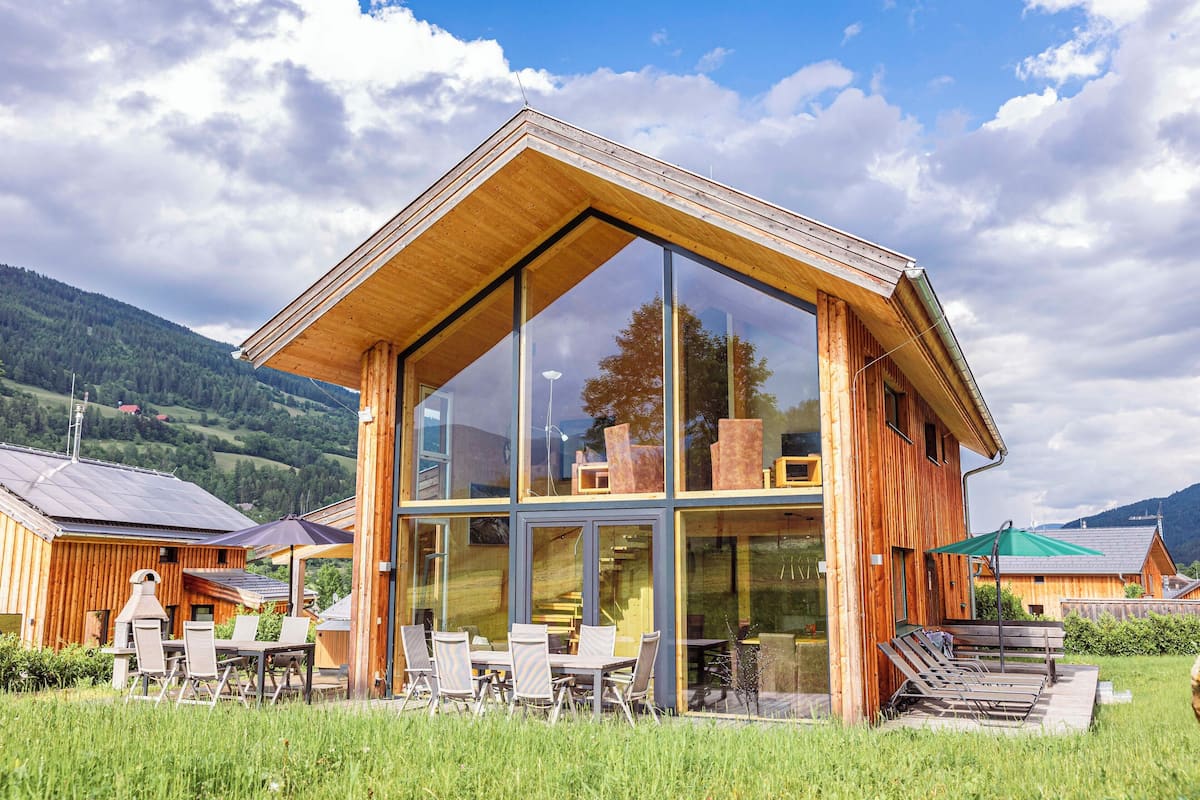 Un edificio moderno de madera con grandes ventanales, asientos al aire libre y vistas del paisaje circundante.