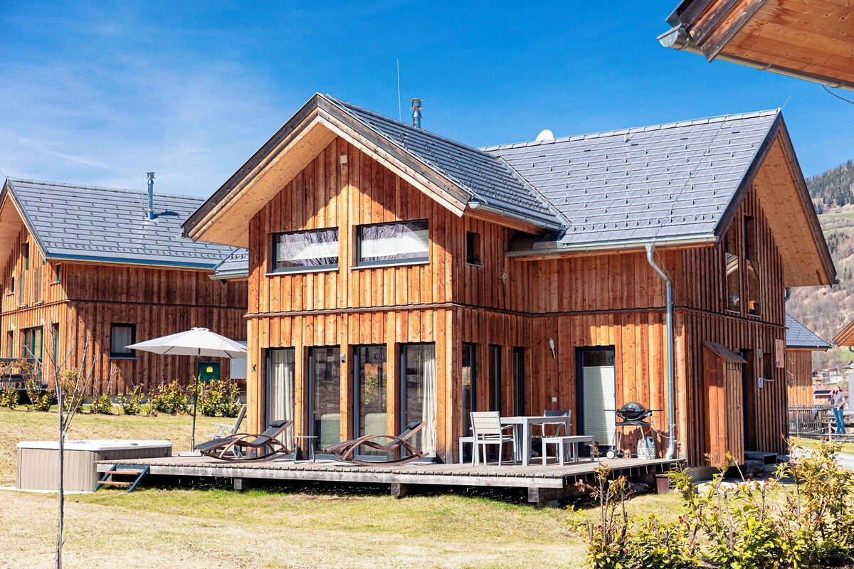 A wooden cabin with a deck, outdoor seating, and a barbecue area.