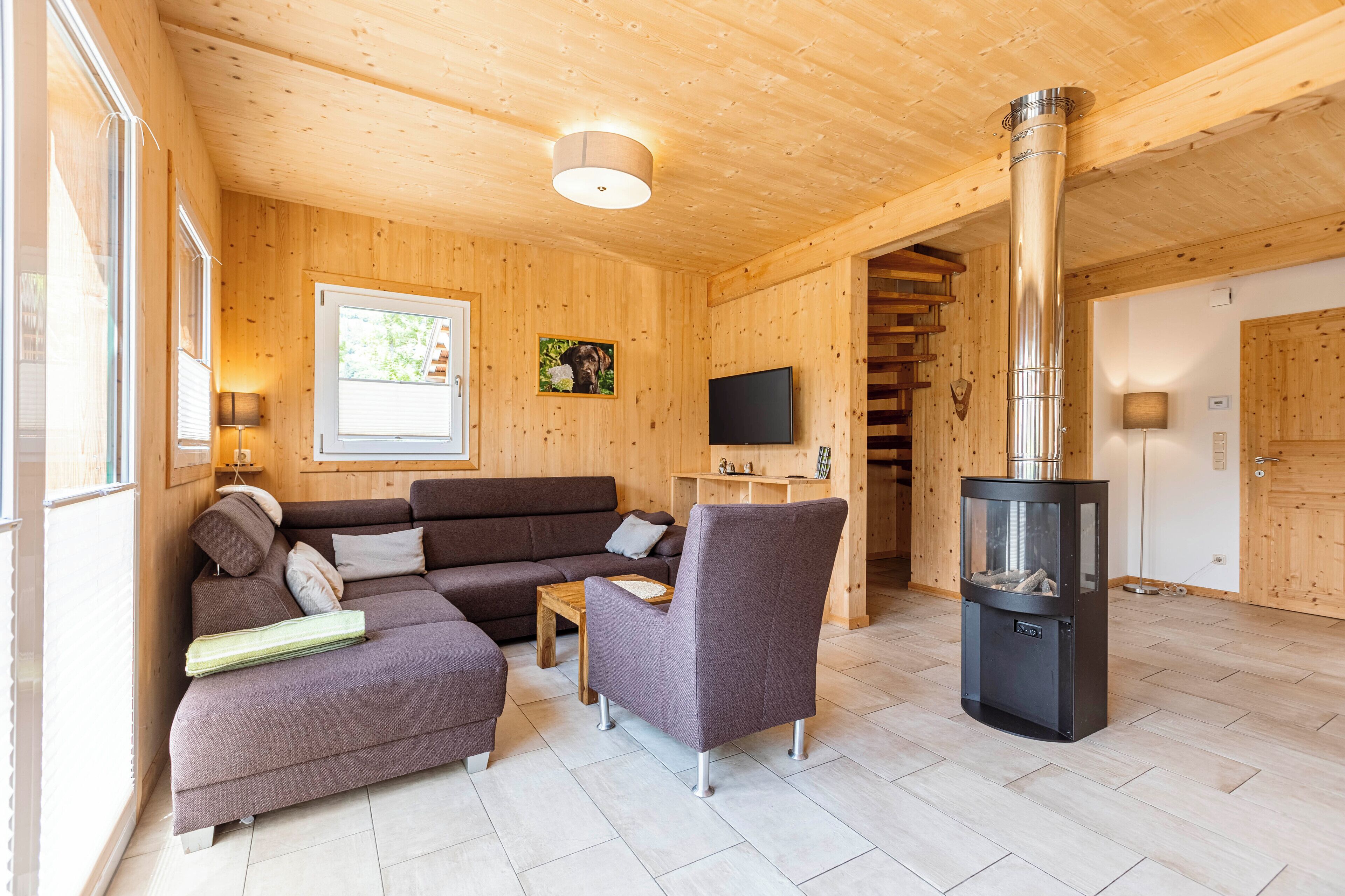 A cozy wooden interior with a sofa, armchair, and a fireplace.