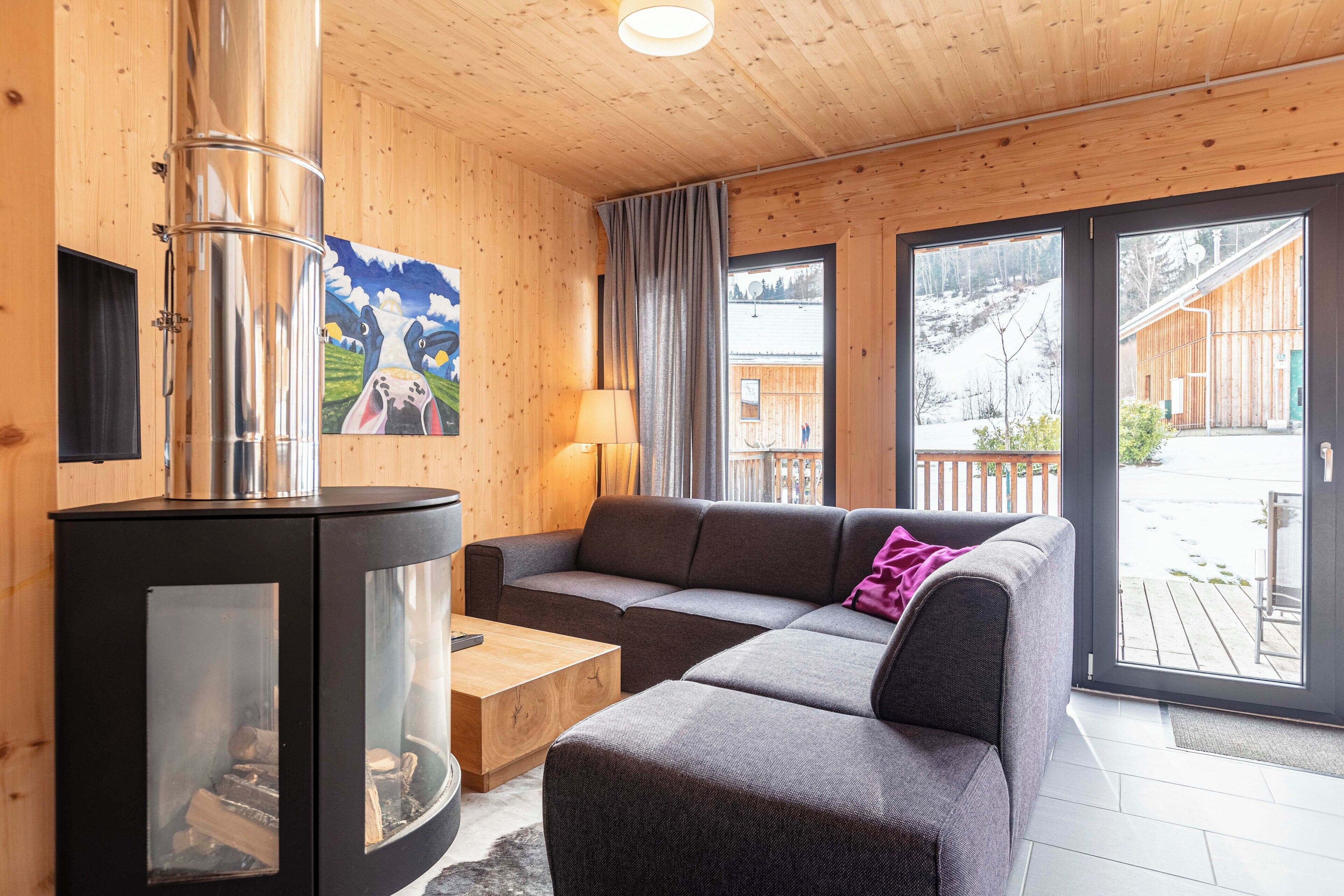 A cozy room with a modern fireplace, a sectional sofa, and large windows offering a view of the outdoors.
