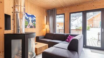 A cozy room with a modern fireplace, a sectional sofa, and large windows offering a view of the outdoors.