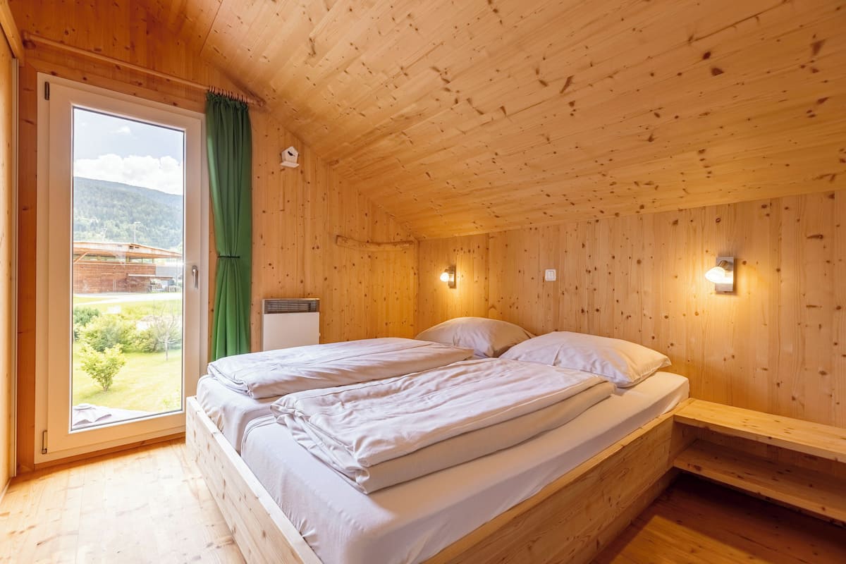 Habitación de cabaña de madera con una cama, una ventana con cortina y vistas a la vegetación.