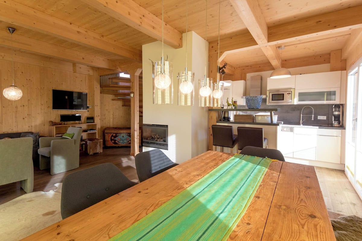A spacious living area with a wooden dining table, comfortable seating, a fireplace, and a kitchen with modern appliances.