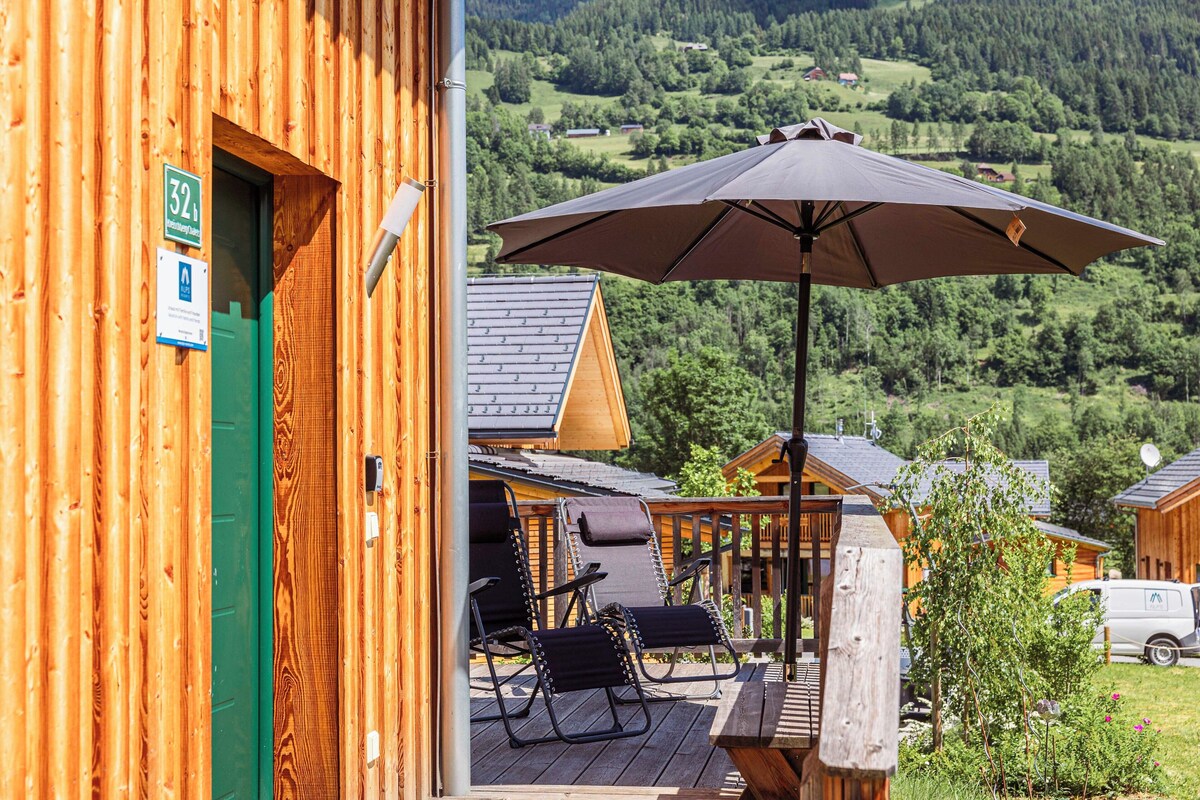 A wooden cabin with a deck, outdoor seating, and a view of a forested valley.