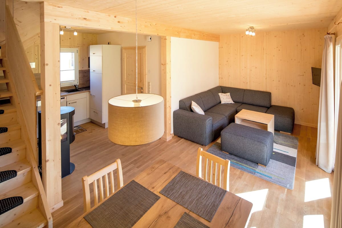 Interior acogedor de una cabaña de madera con comedor, sofás y cocina.