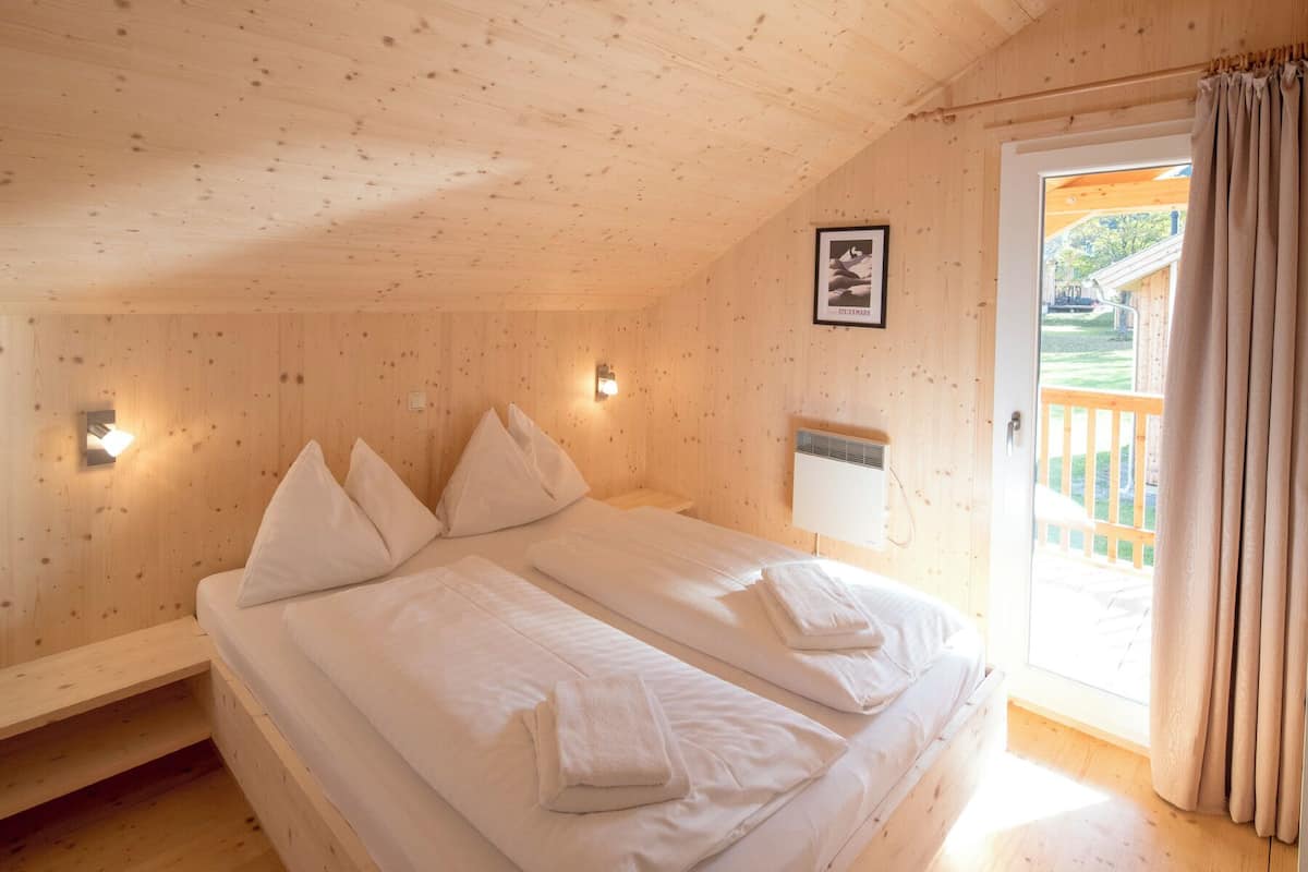 A wooden cabin bedroom with a bed, pillows, a wall-mounted light, and a picture.