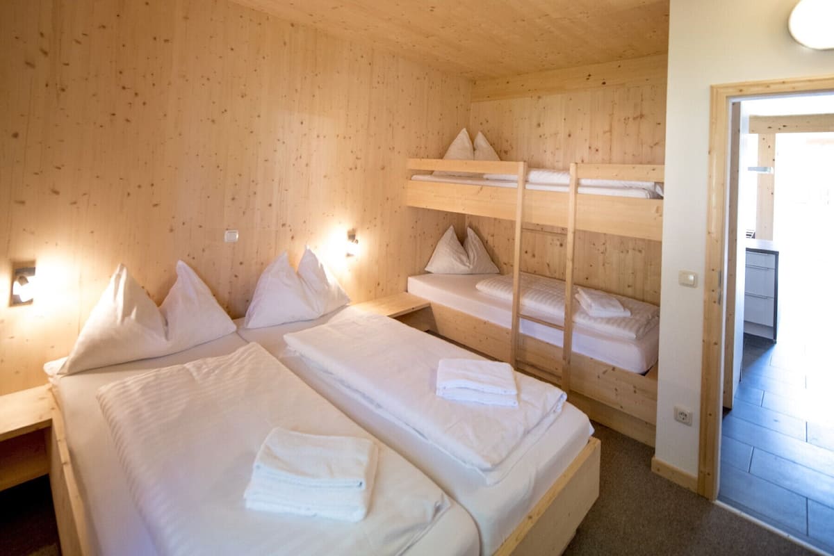 Una habitación con literas, paredes de madera y una puerta que da a otra zona.