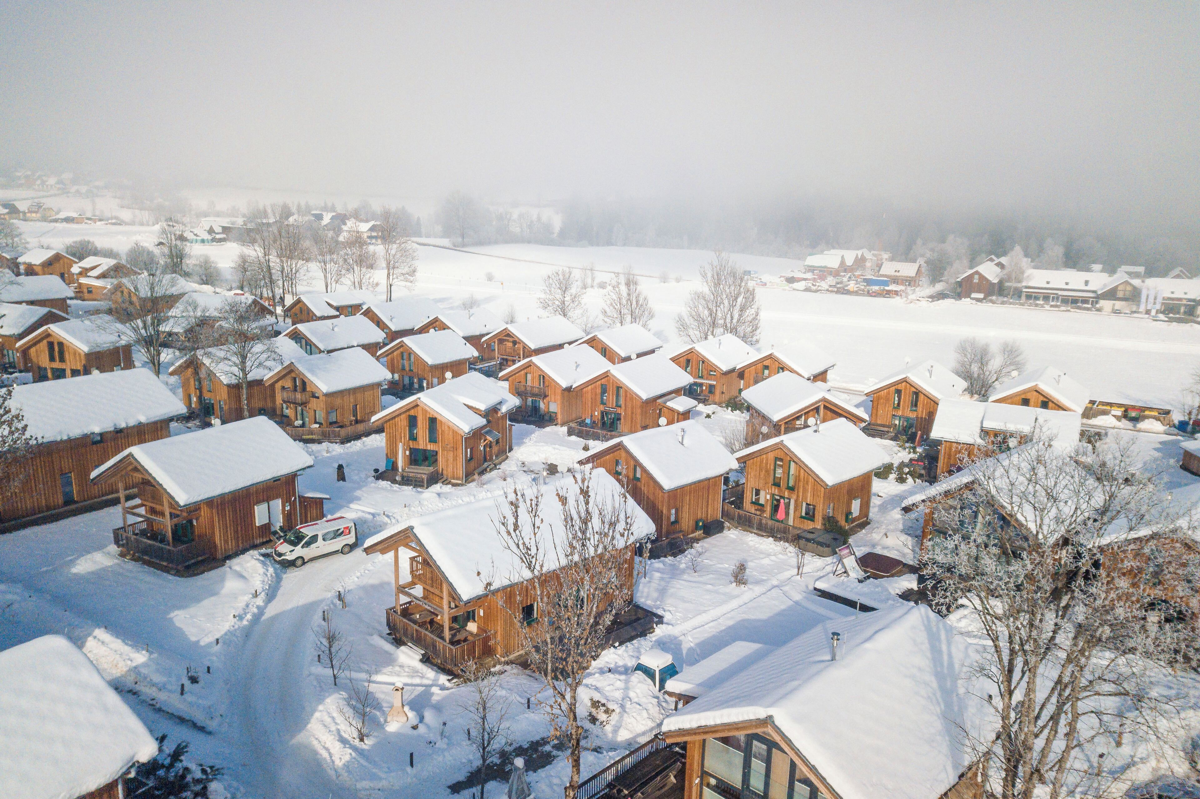 Un pueblo cubierto de nieve con cabañas de madera, cielo despejado y una vista distante de un pueblo.
