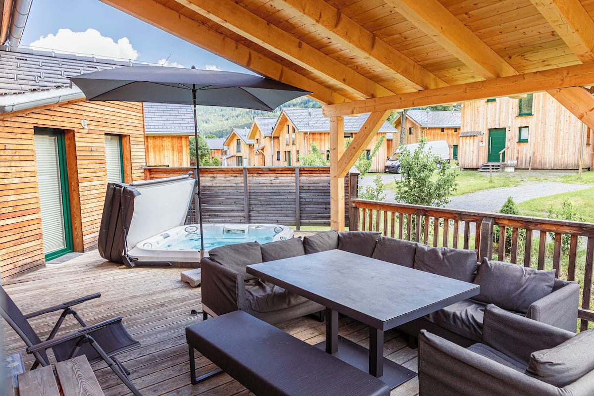 Terraza de madera con jacuzzi, asientos exteriores y zona cubierta.