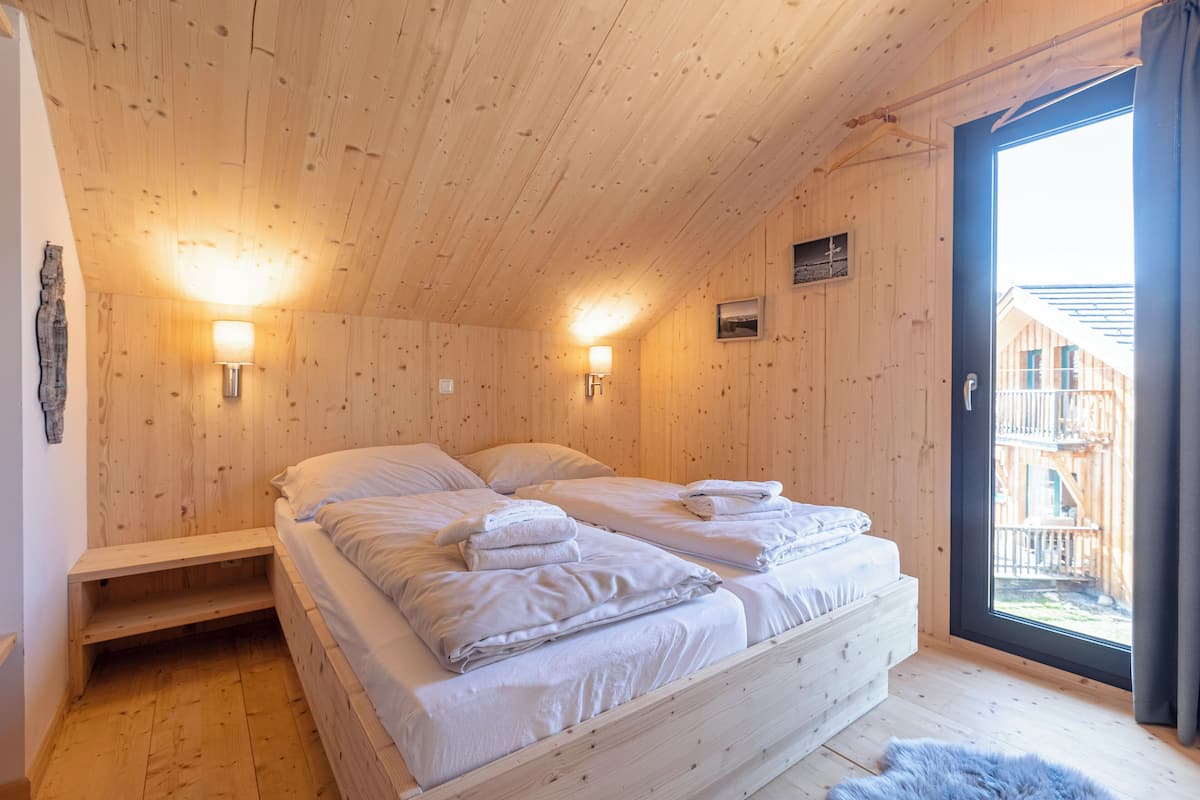 Un dormitorio de cabaña de madera con dos camas, un banco y un ventanal grande.