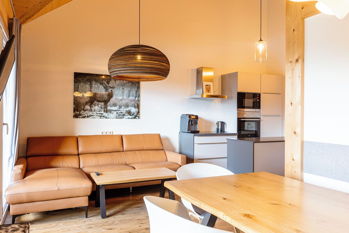 A modern kitchen with a sofa, dining table, and a painting of deer on the wall.