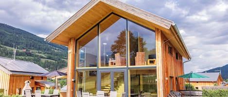 Un edificio moderno de madera con grandes ventanales, asientos al aire libre y vistas del paisaje circundante.