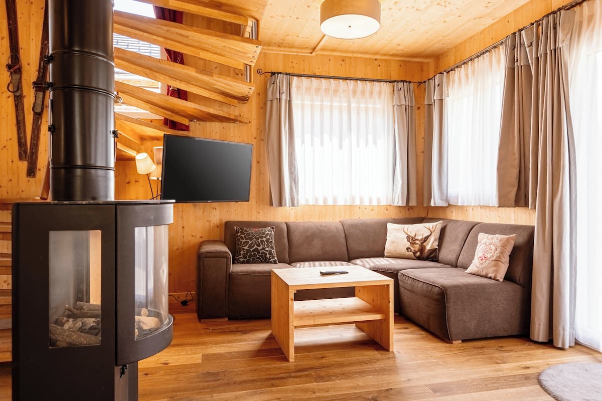 Interior acogedor de una cabaña de madera con estufa de leña, un sofá y un televisor de pantalla plana.