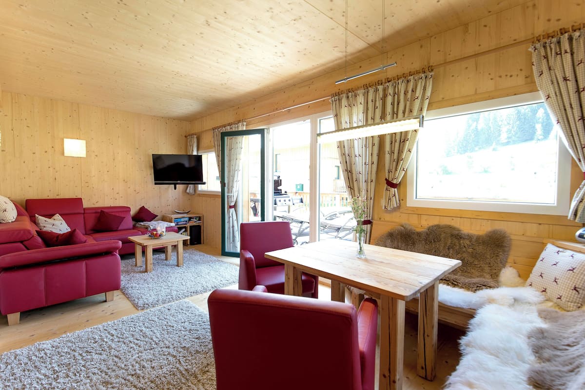Un acogedor interior de cabaña con un sofá rojo, una mesa de madera y un televisor montado en la pared.