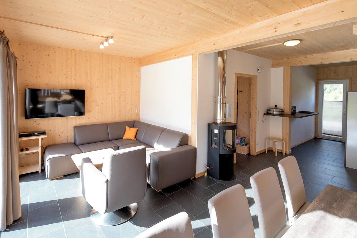 A modern living room with a sectional sofa, a flat-screen TV, a fireplace, and a kitchen area with a refrigerator and a small table.