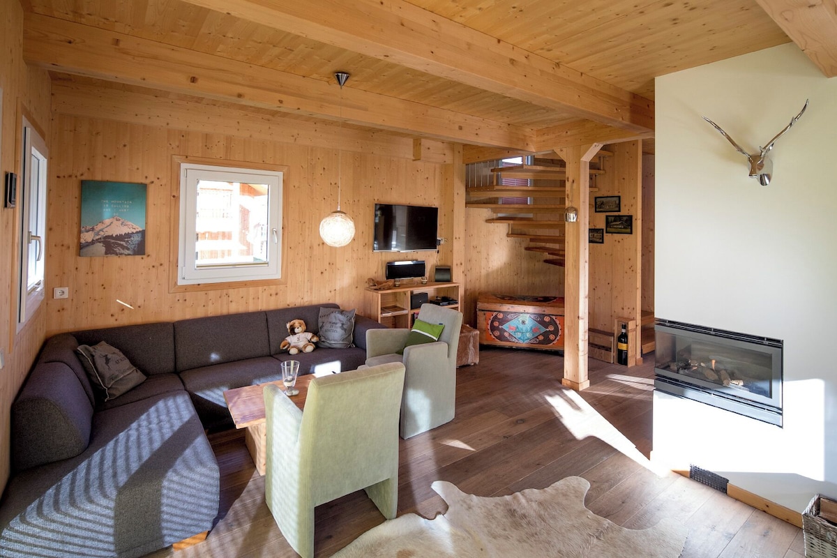 A cozy wooden interior with a sofa, a television, a fireplace, and a dining area.