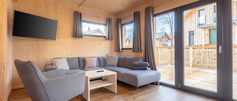 Een moderne woonkamer met een grijze modulaire bank, een houten salontafel en een flatscreen televisie die aan de muur is bevestigd.
