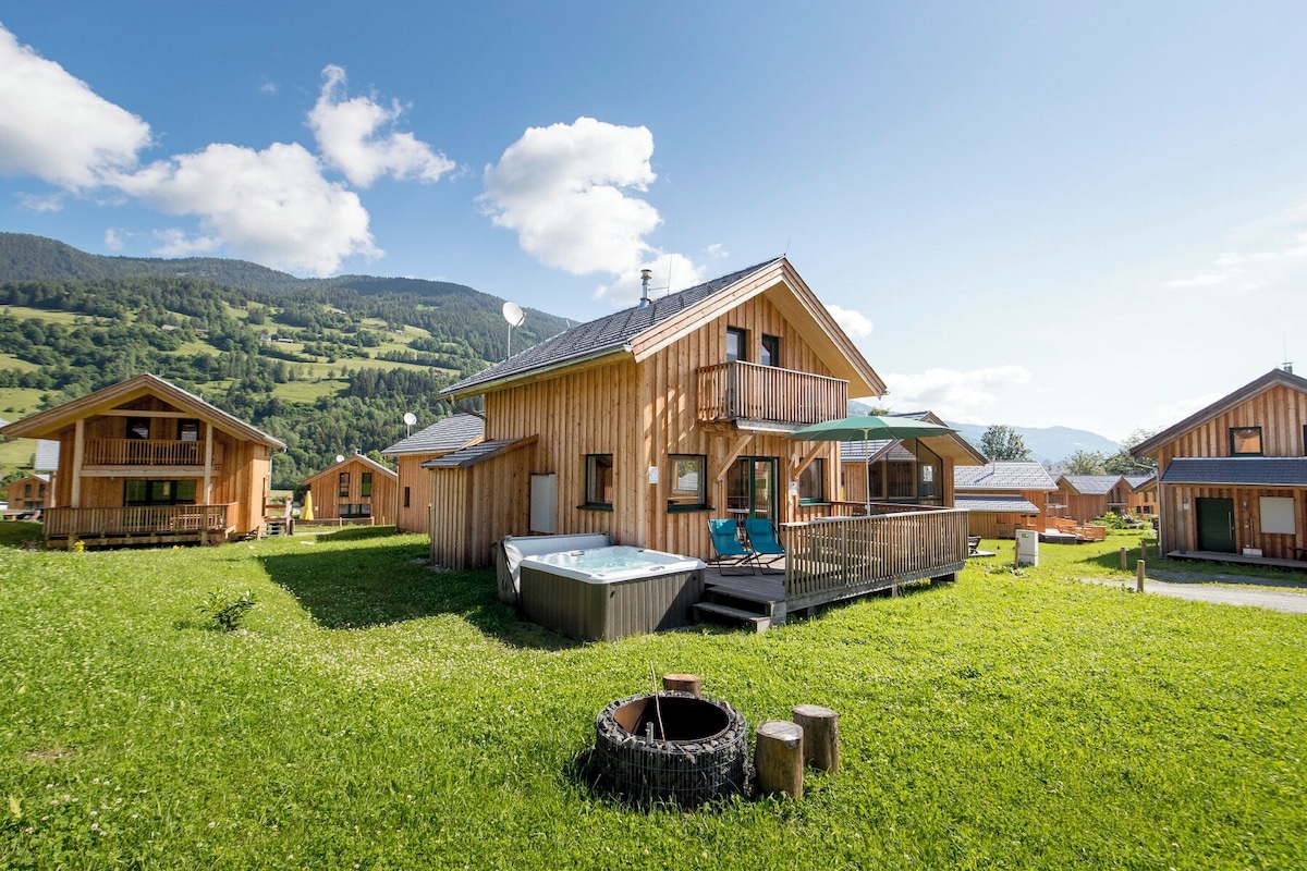 A wooden chalet with a hot tub, deck, and a view of mountains.