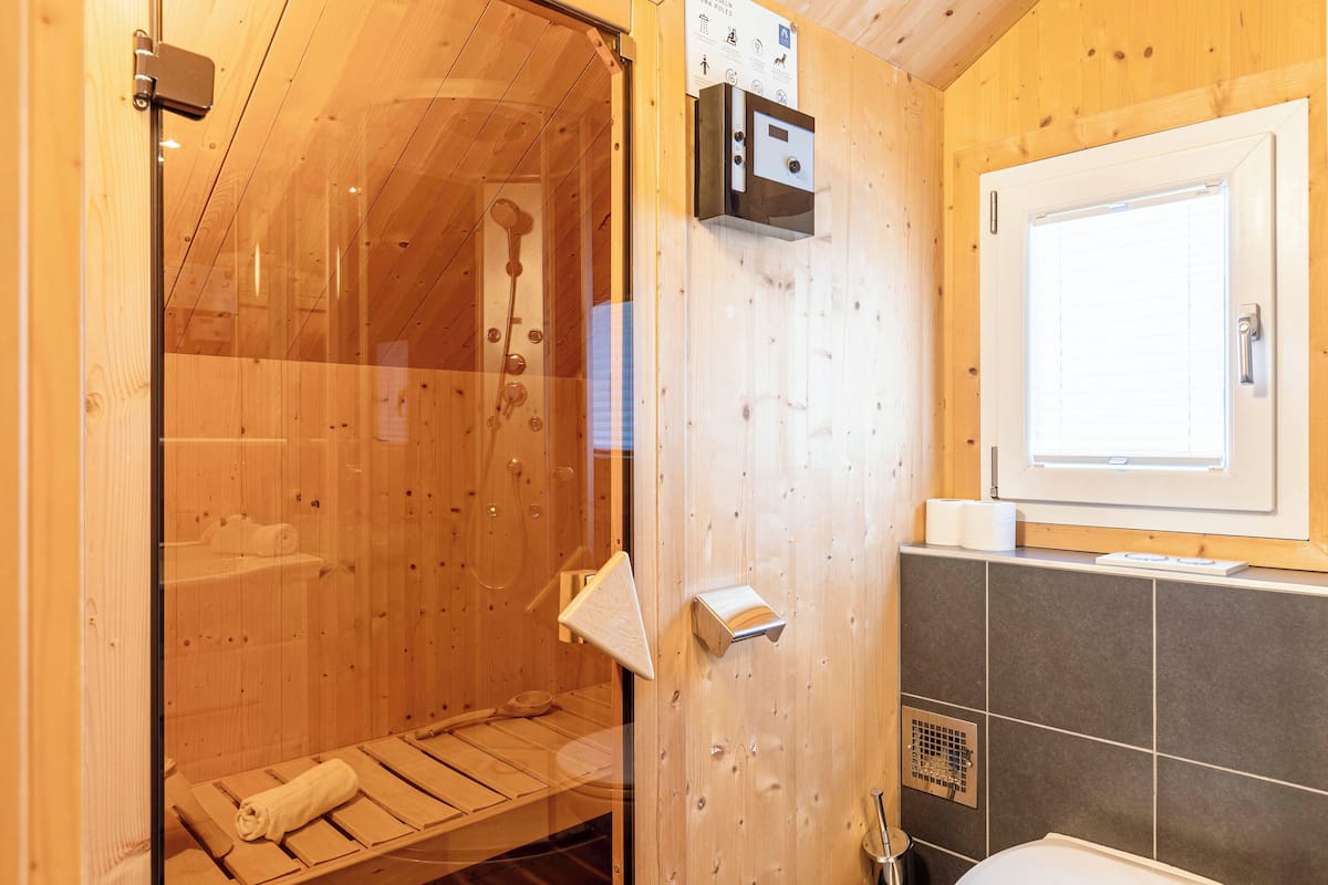 A wooden sauna room with a glass door, a towel rack, and a window.