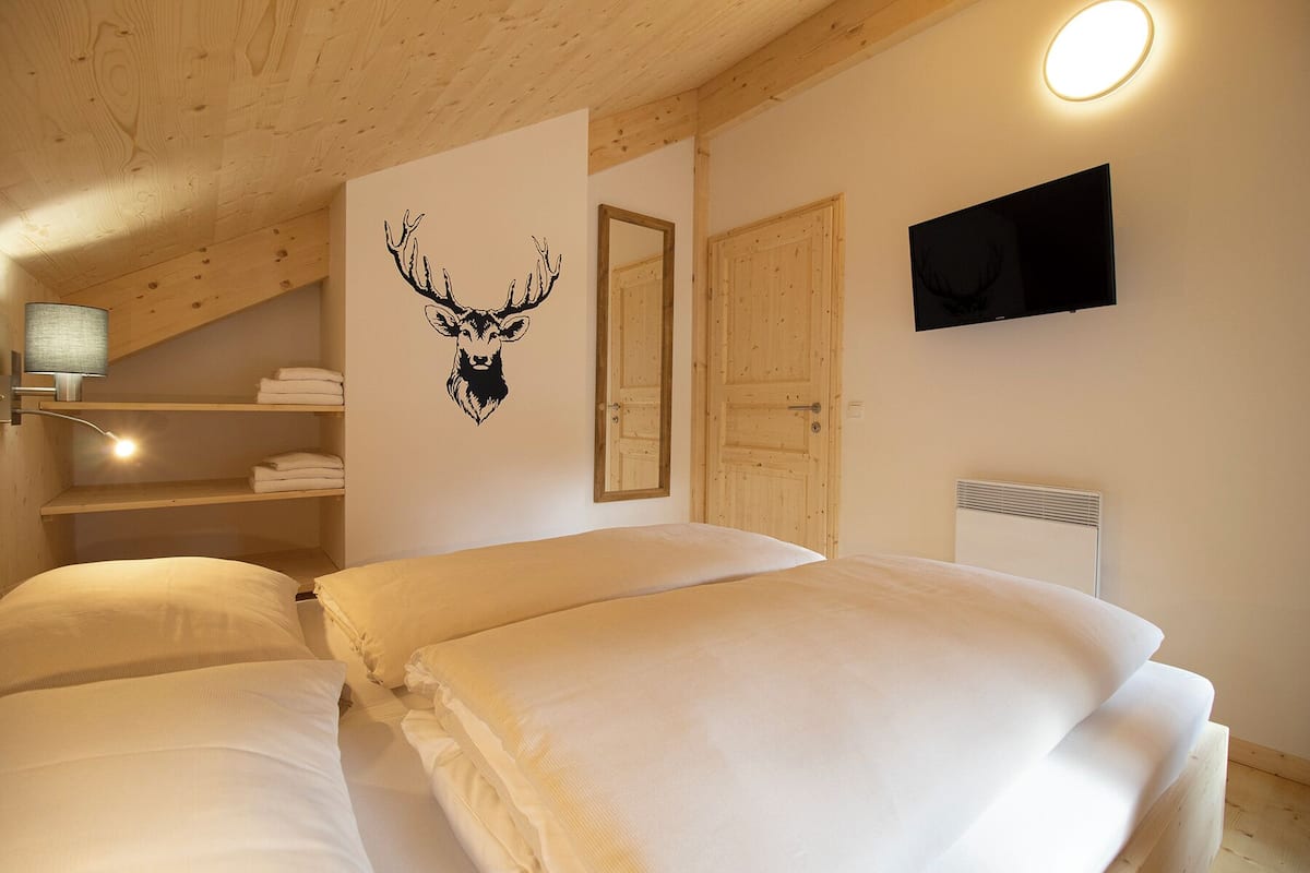 Un dormitorio con dos camas, un televisor montado, una puerta de madera y un espejo fijado a la pared.