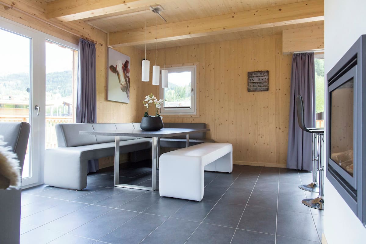 A modern interior with a wooden ceiling, a dining area with a bench, a table, and a large window.