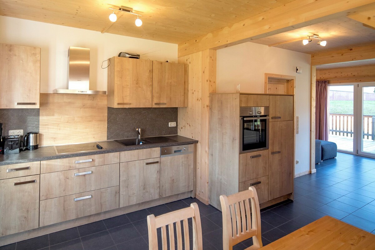 A modern kitchen with wooden cabinets, a built-in oven, and a dining area with a wooden table and chairs.