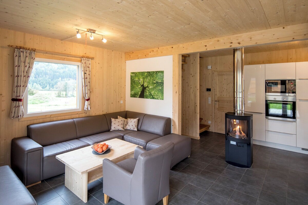 A modern cabin interior with a wooden interior, a sofa set, a coffee table, a fireplace, and a kitchen area.