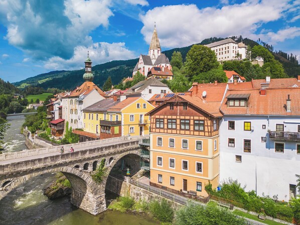 A historic town with a stone bridge over a river, colorful buildings, and a church with a tall spire. - Kreischberg Chalets by ALPS RESORTS (Sankt Georgen am Kreischberg)