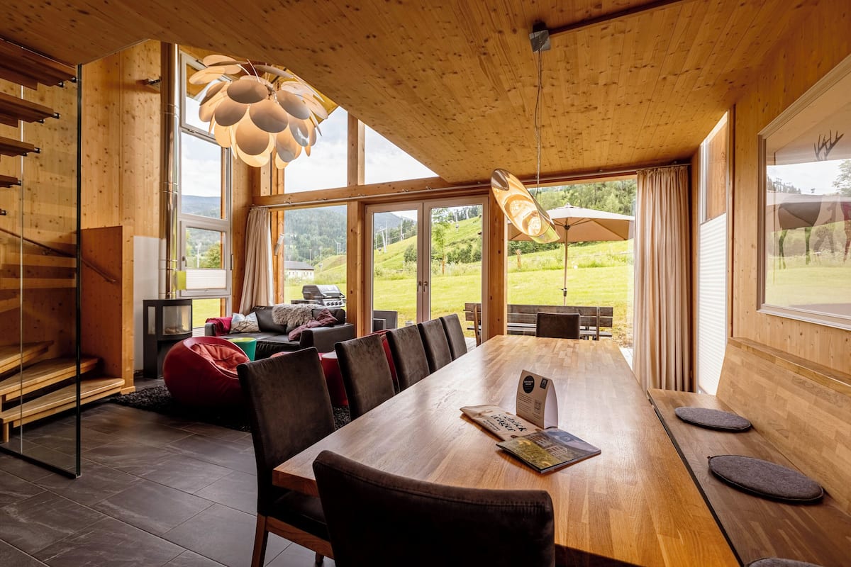 A spacious dining area with a long wooden table, multiple chairs, and a large window offering a view of the outdoors.