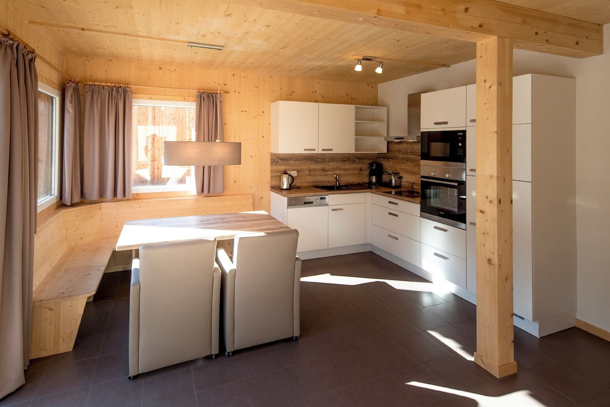 A modern kitchen with wooden accents, a built-in oven, and a dining area with a bench.