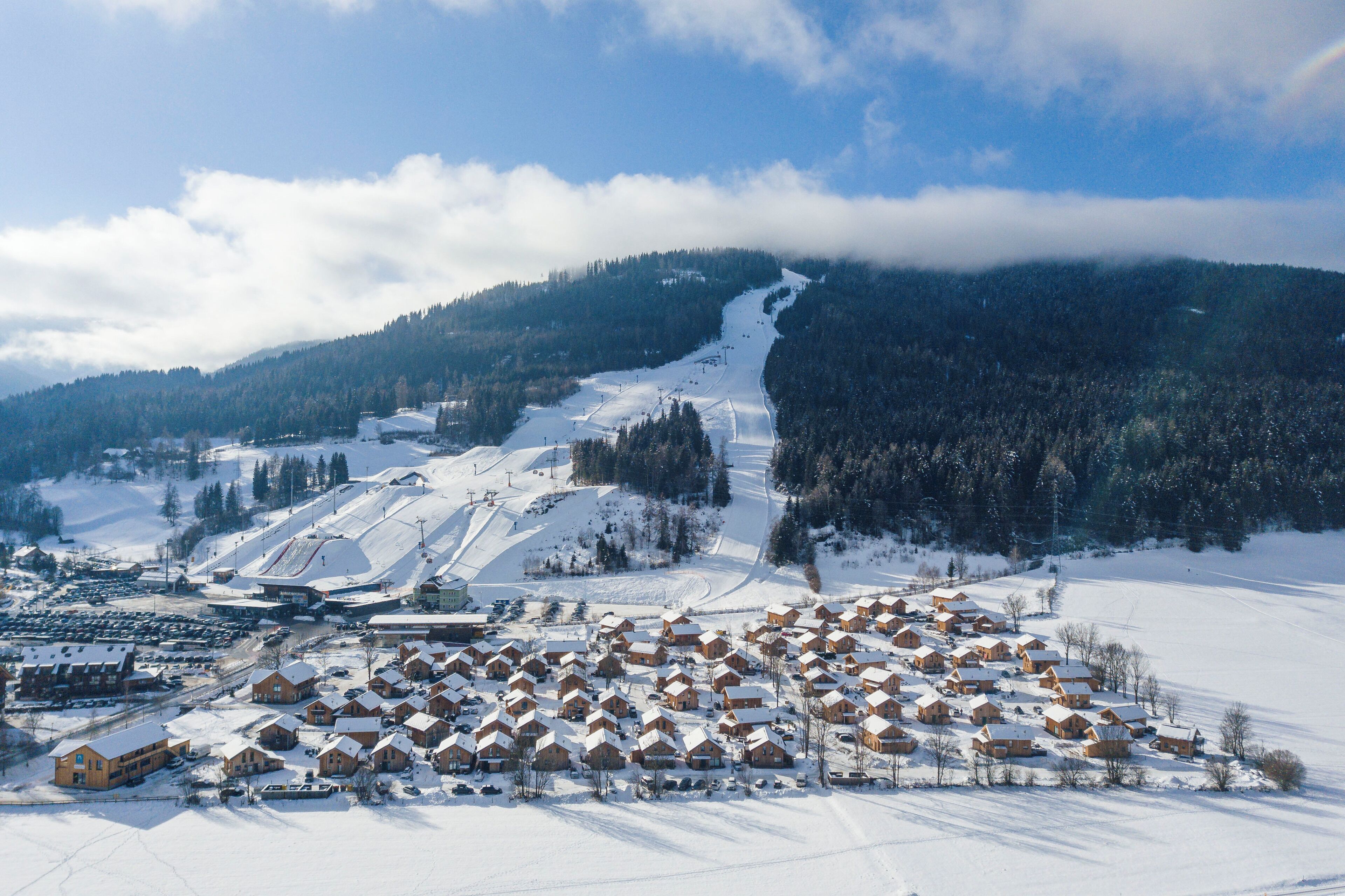 A snow-covered village with wooden houses and a ski slope in the background.