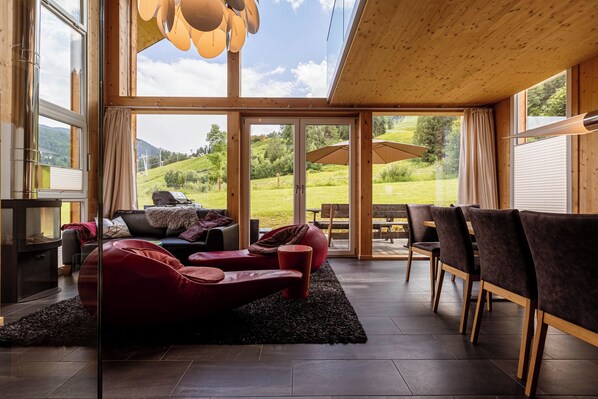 A modern living room with a fireplace, red leather sofa, and a dining area with chairs and a table. - Kreischberg Chalets by ALPS RESORTS (Sankt Georgen am Kreischberg)