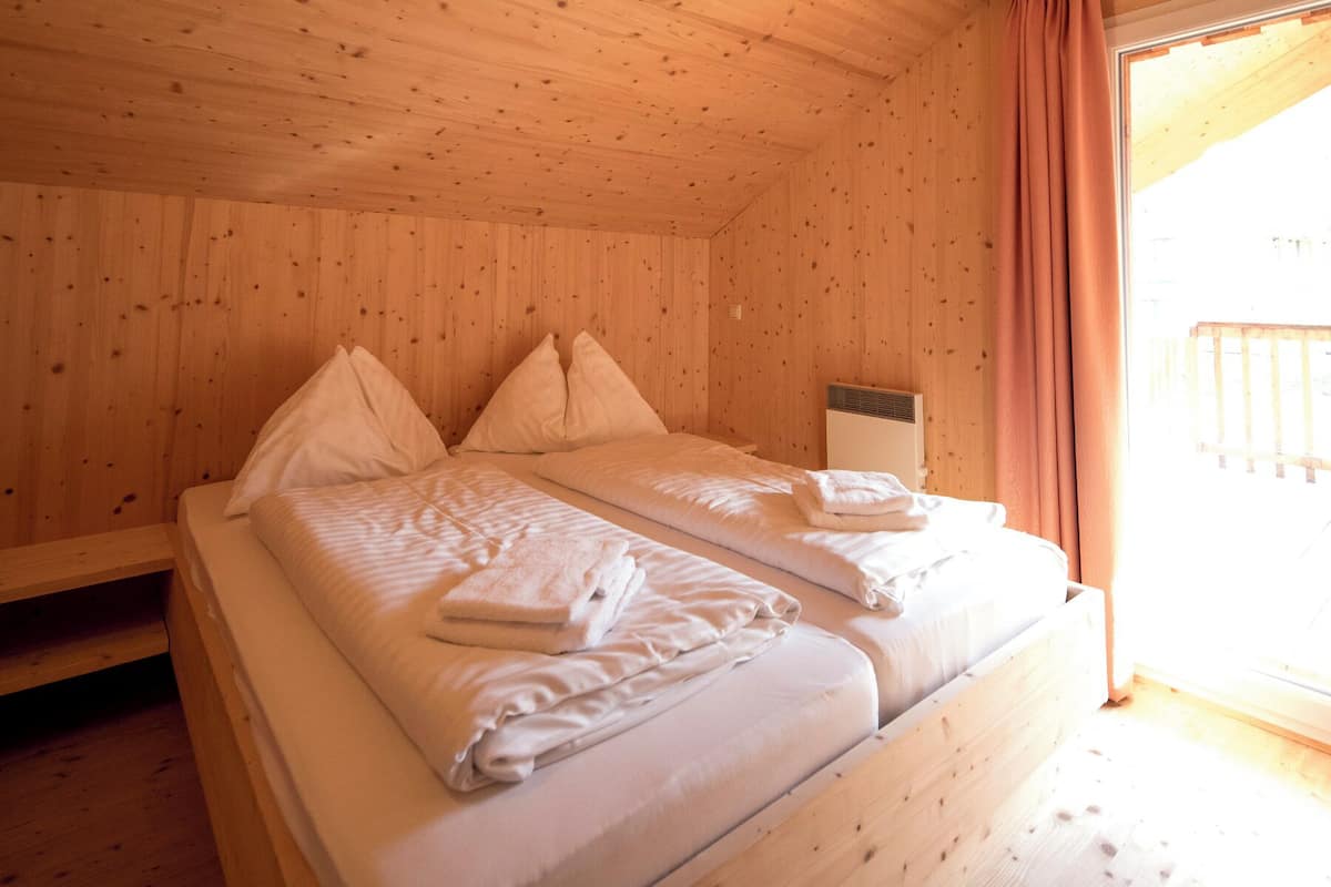 A wooden room with a bed, pillows, and a window with curtains.