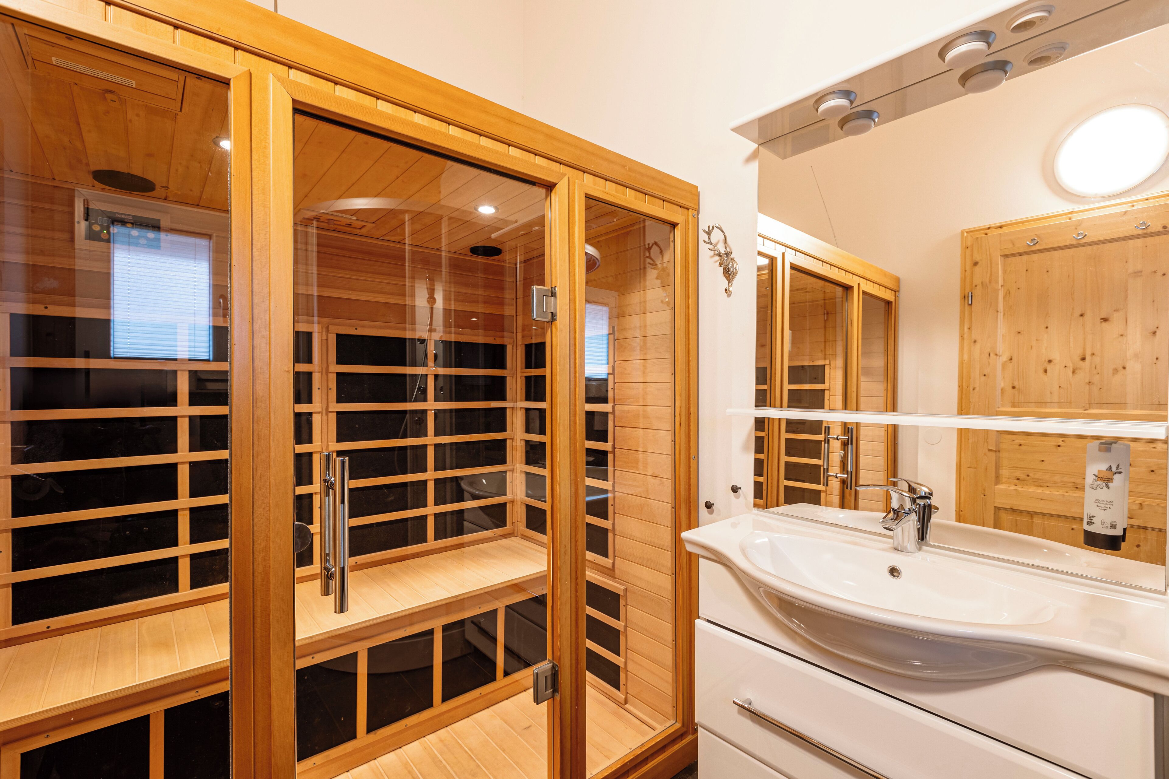 A modern bathroom with a wooden sauna, a large sink, and a mirror.