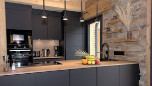 A modern kitchen with dark cabinetry, a wooden countertop, and a stone accent wall. - Kreischberg Chalets by ALPS RESORTS (Sankt Georgen am Kreischberg)