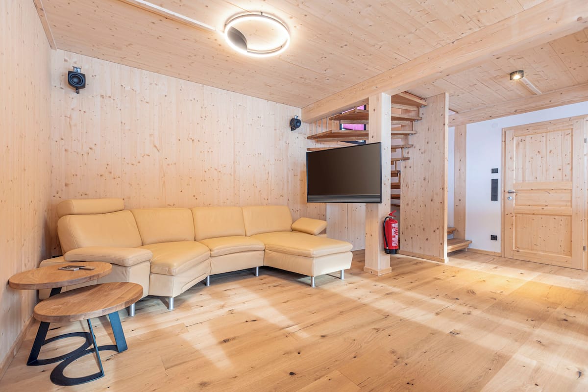 Un salón con suelo de madera, un sofá seccional color beige, un televisor de pantalla plana y una pequeña mesa de madera.