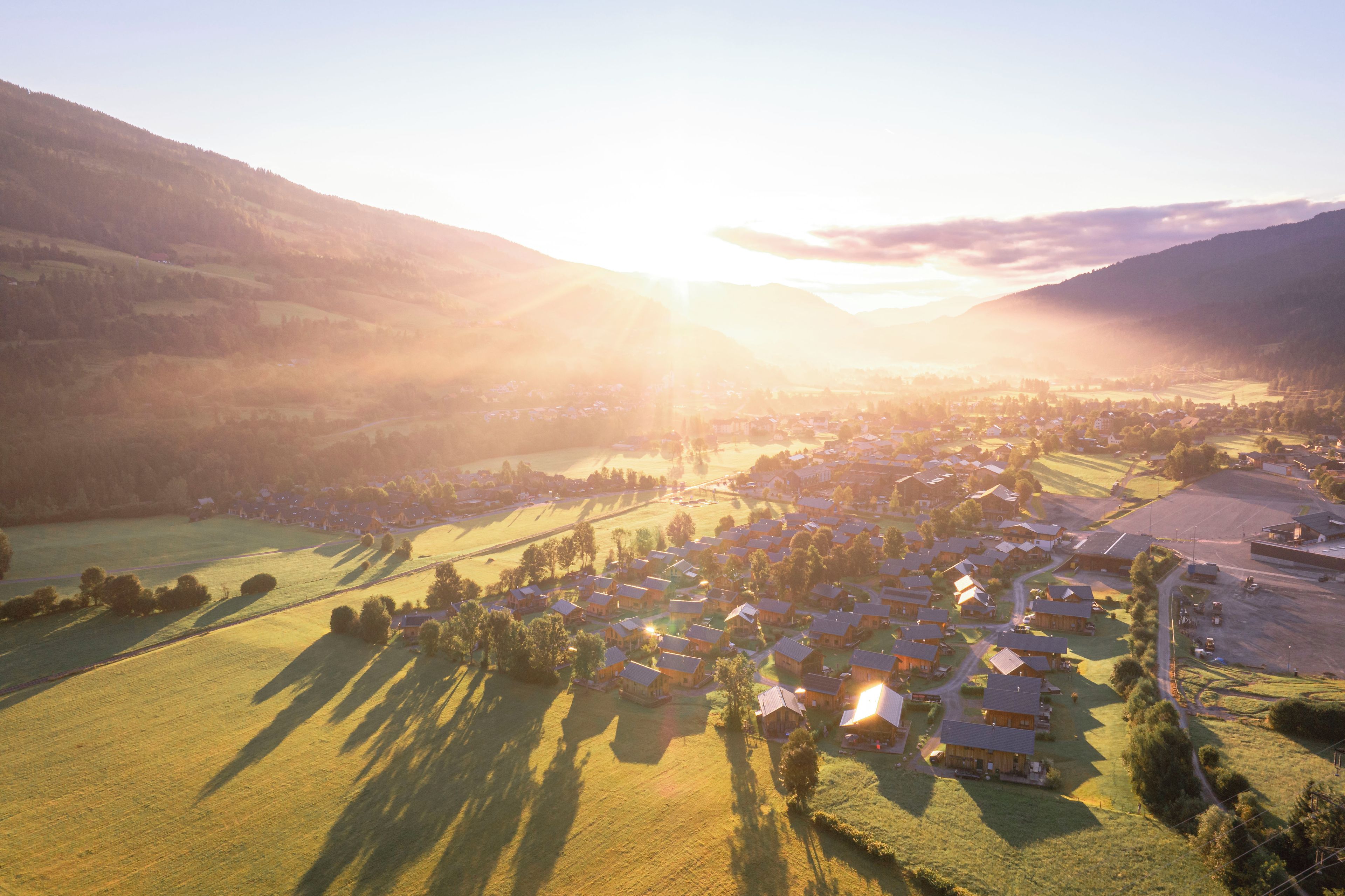 A rural village with houses and fields, surrounded by hills.