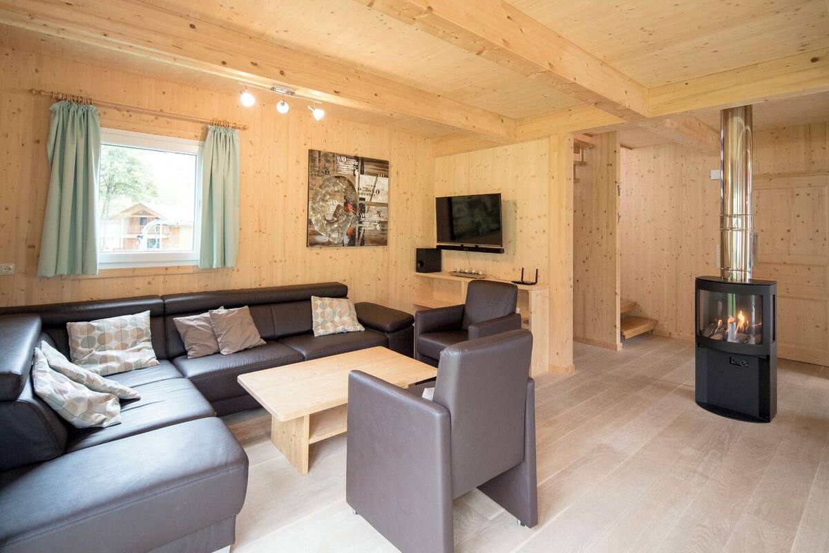 A wooden interior with a sofa, coffee table, and chairs, a TV, and a fireplace.