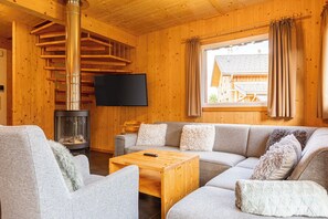 A cozy cabin interior with a wooden interior, a sofa, a television, and a fireplace. - Kreischberg Chalets by ALPS RESORTS (Sankt Georgen am Kreischberg)