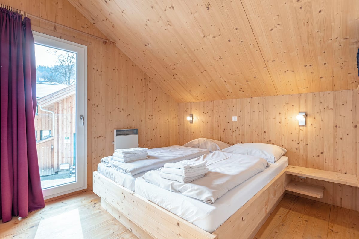 Habitación de cabaña de madera con cama, un banco y una ventana con cortinas.