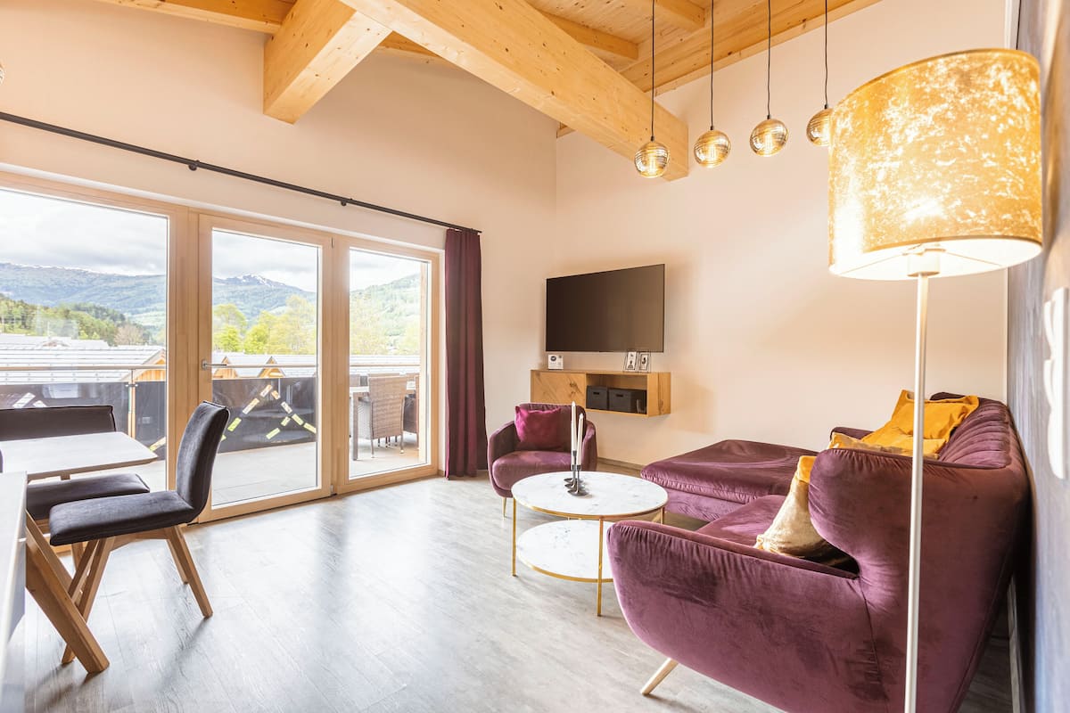 A modern living room with a large window, a flat-screen TV, and a purple sofa.