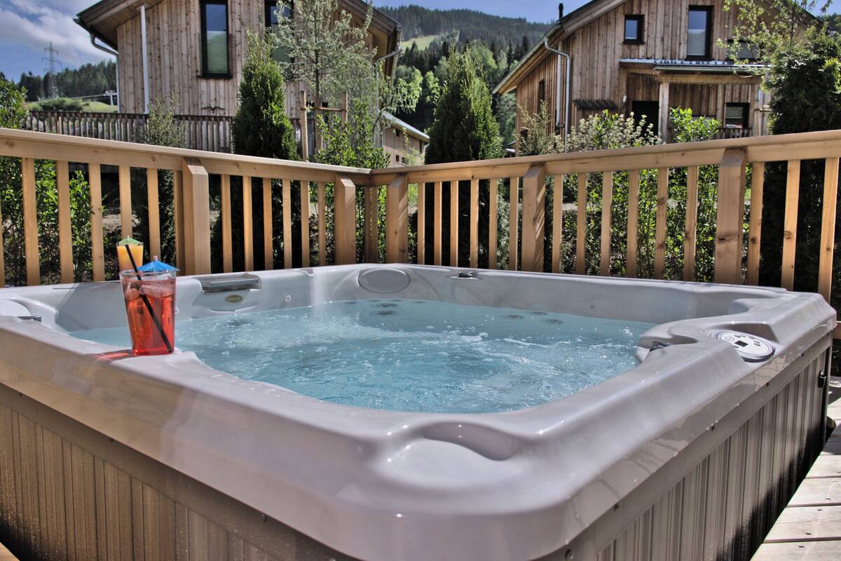 Un jacuzzi en una terraza de madera con vistas a casas de madera y árboles al fondo.
