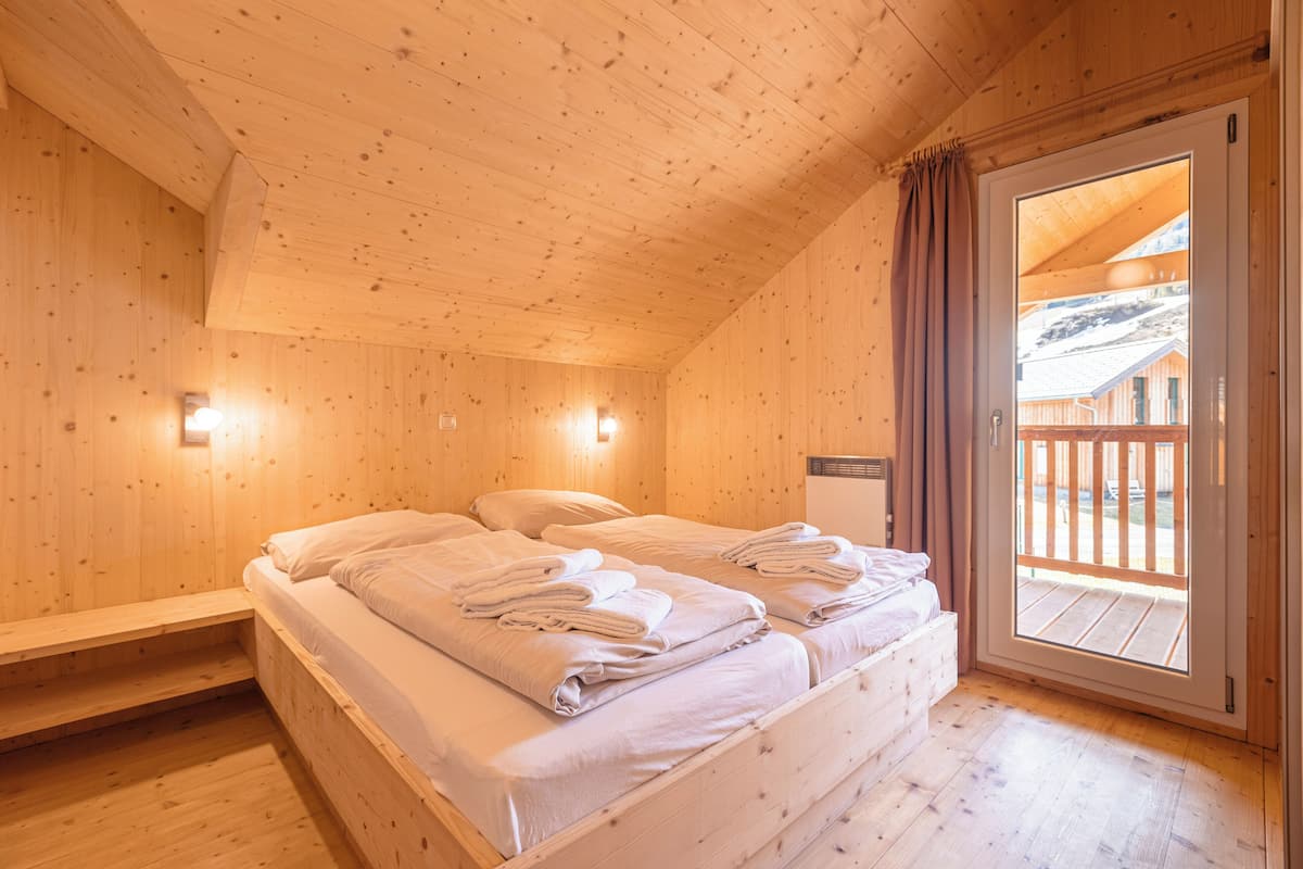 Una habitación de cabaña de madera con una cama, un banco y una puerta que da a un espacio exterior.
