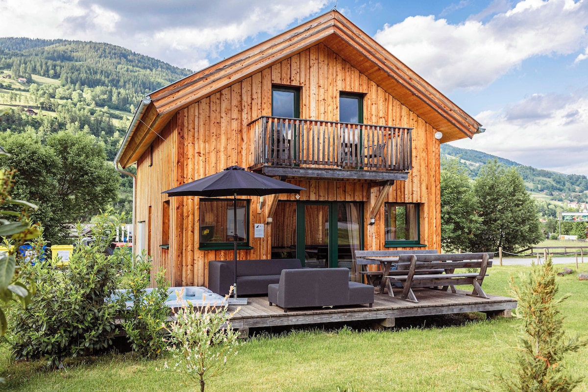 A wooden cabin with a balcony, outdoor seating, and a view of the surrounding landscape.